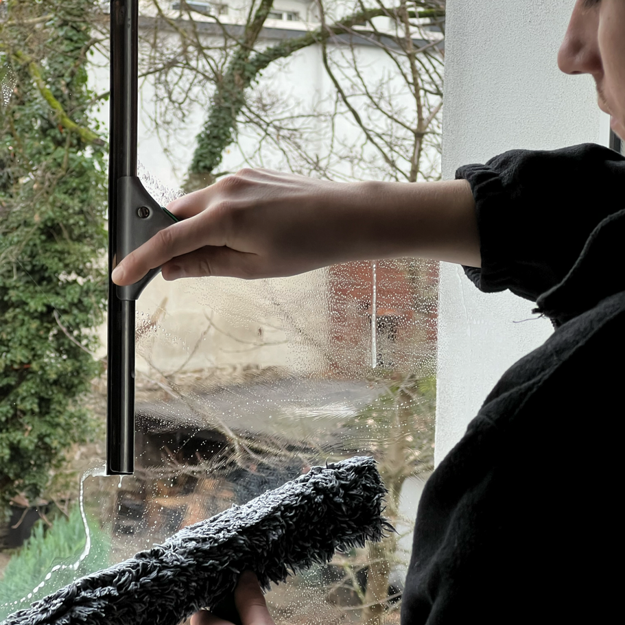 Junger Mann der eine Glasscheibe mithilfe eines Einseifers und eines Abziehens streifenfrei in Wuppertal putzt.