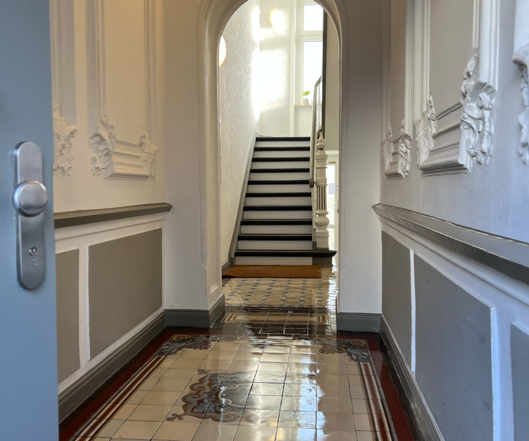 Heller Eingangsbereich eines Treppenhauses mit Fliesenboden und Treppe